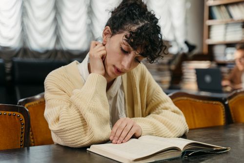 Free A woman deeply engaged in reading at a library table, surrounded by books. Stock Photo