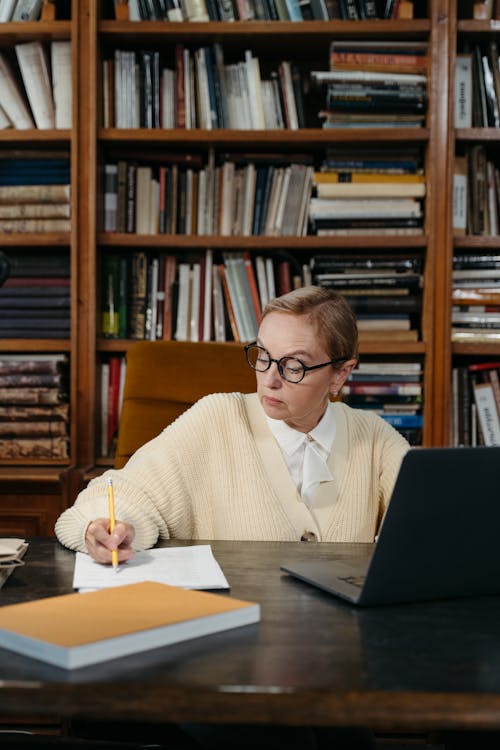 An Elderly Woman Taking Notes while Sitting behind a Desk 