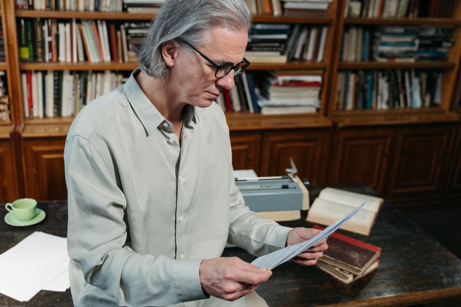 Senior man with gray hair reading documents in a cozy library.