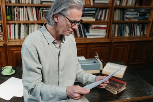 Free Senior man with gray hair reading documents in a cozy library. Stock Photo