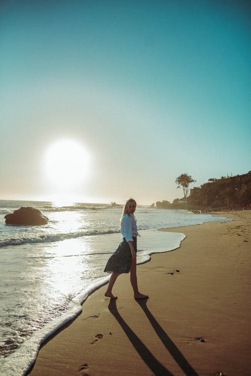 Free Pretty Woman Wearing White Long Sleeves Walking on the Beach Stock Photo