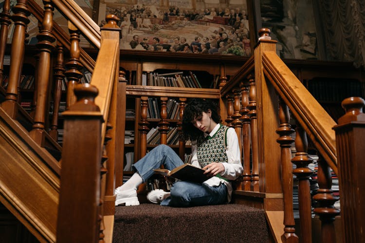 A College Student Reading A Book White Sitting On The Stairs