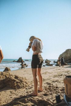Female photographer taking photos at a sunny beach with a DSLR camera in hand.