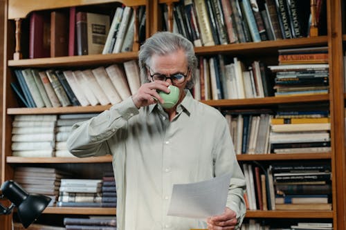 Free A Elderly Man Drinking on a Ceramic Cup while Reading a Document Stock Photo
