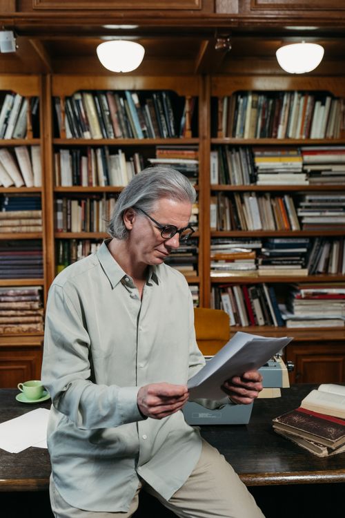Free An elderly man reads papers in a cozy library filled with books. Stock Photo