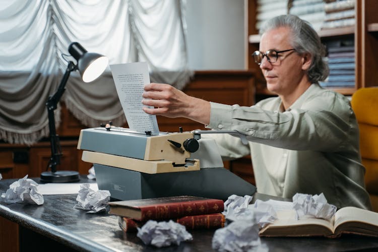 A Man Removing A Paper On A Vintage Typewriter