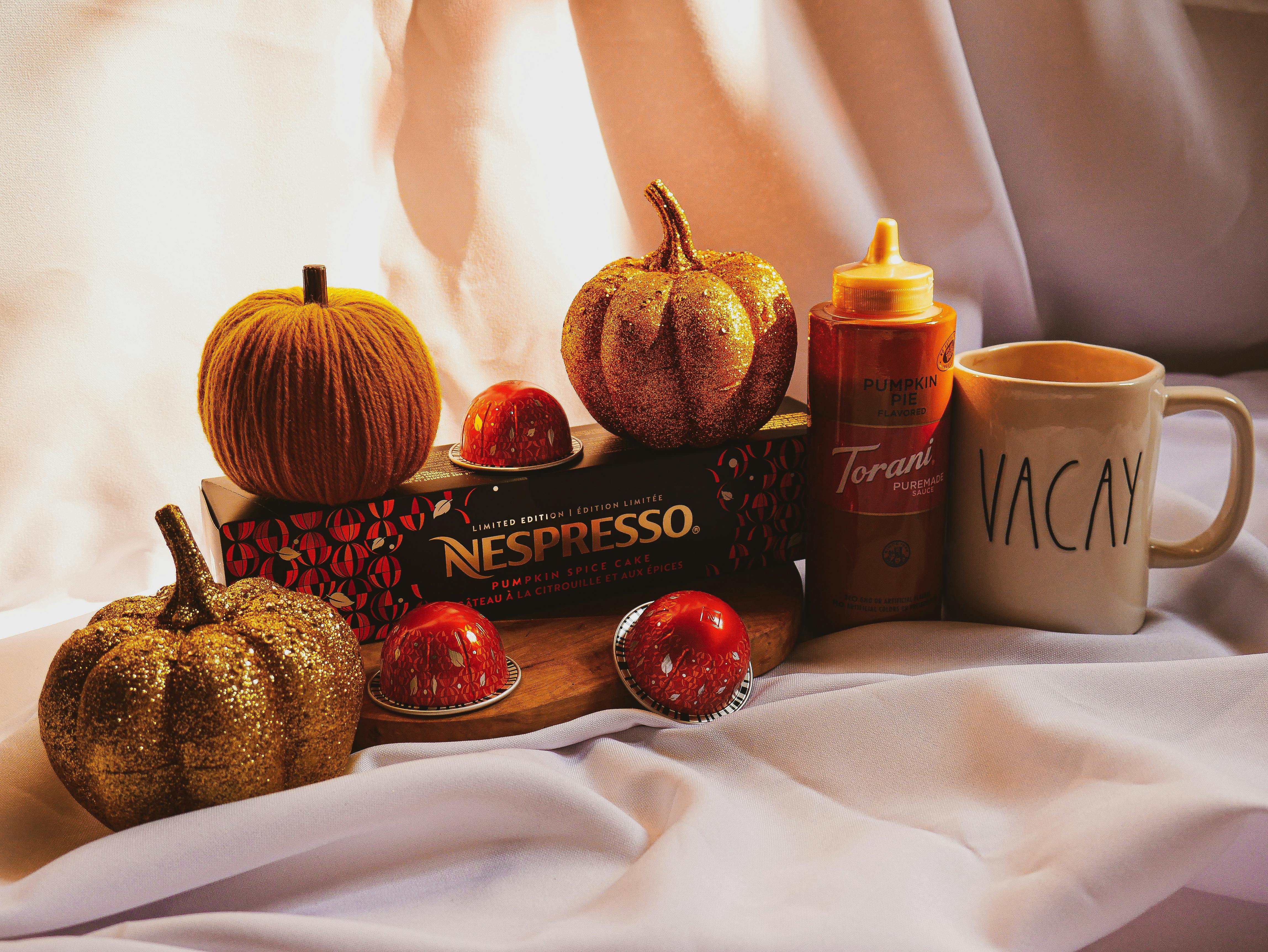 A warm autumn-themed coffee arrangement featuring Nespresso capsules, pumpkins, and a mug.