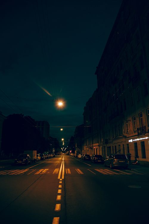 Free Quiet urban street at night with parked cars and glowing streetlights, creating a moody ambiance. Stock Photo