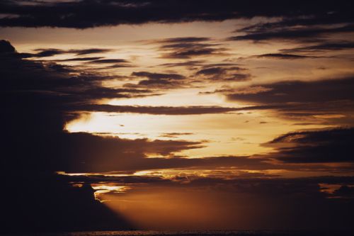 Free Capture of a vibrant sunset over the ocean, highlighting dark clouds and golden hues. Stock Photo