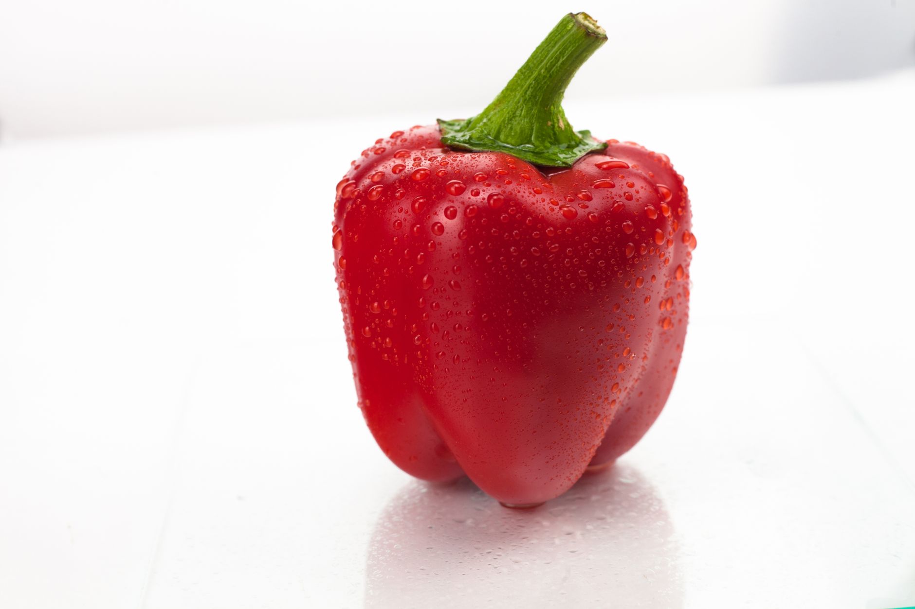 Close-up shot of a fresh red bell pepper with water droplets on a white background.