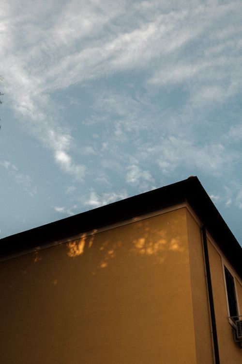 Free A low angle shot of a yellow building against a blue sky with scattered clouds. Stock Photo