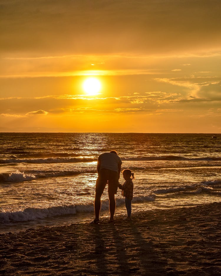 Man With His Daughter On A Beach At Sunset