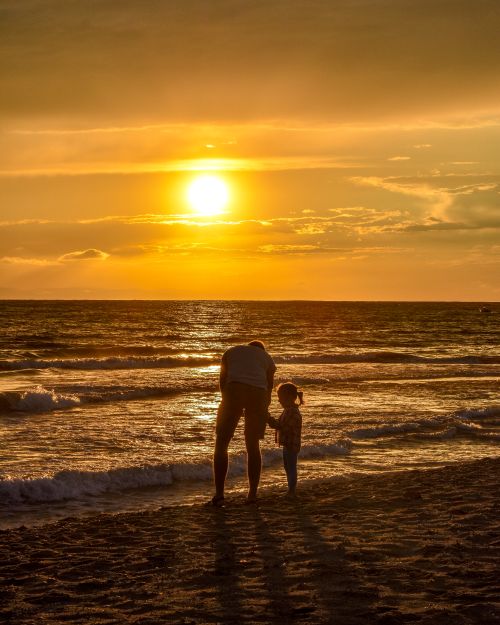 Free A touching scene of a father and daughter walking along a Greek beach during sunset, casting long shadows. Stock Photo