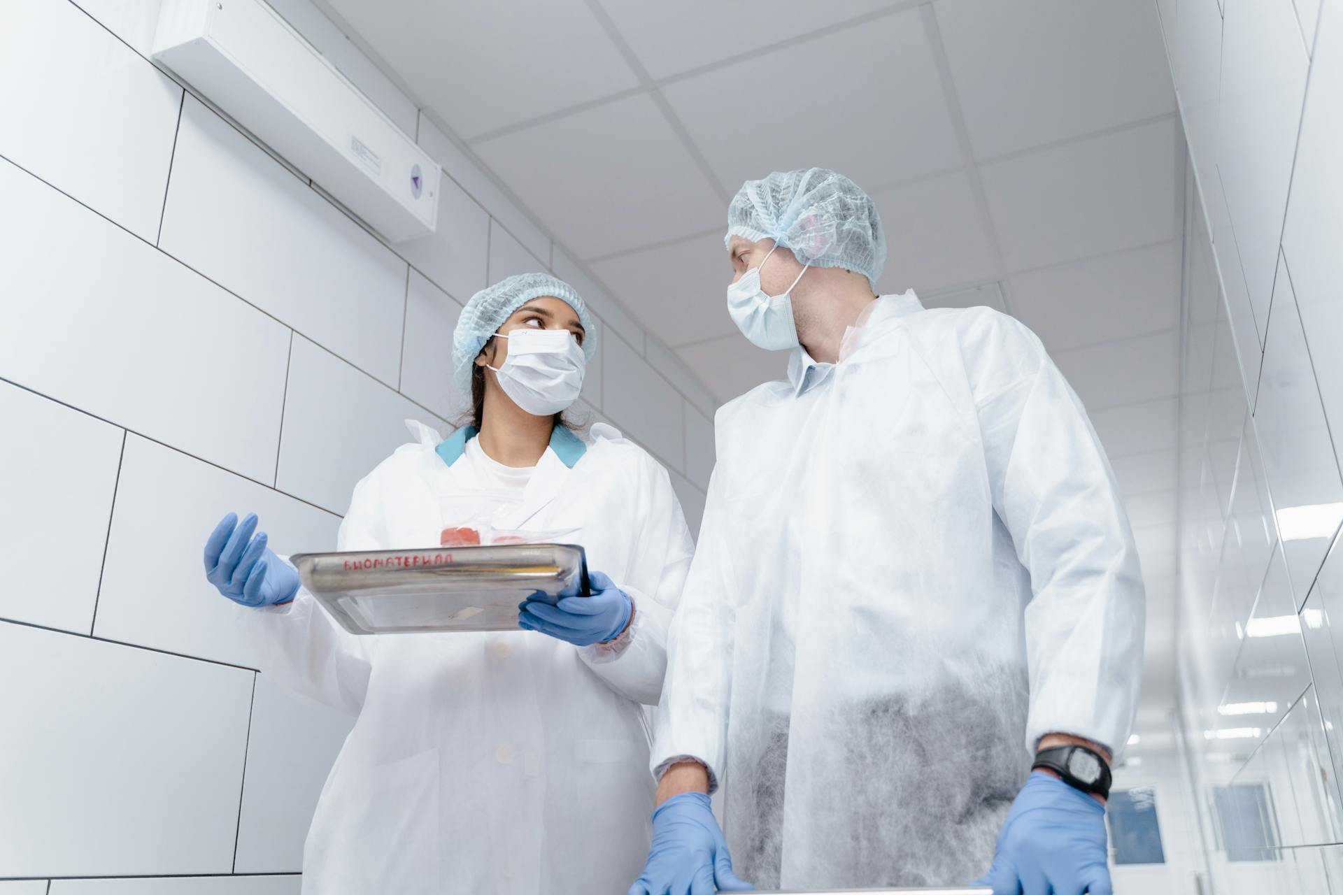 Two medical professionals in protective gear conversing in a laboratory hallway.