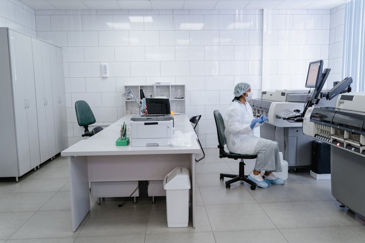 A Woman In White Lab Gown Looking At The Screen