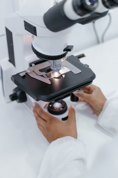 Scientist's hands operating a microscope in a laboratory setting for research purposes.