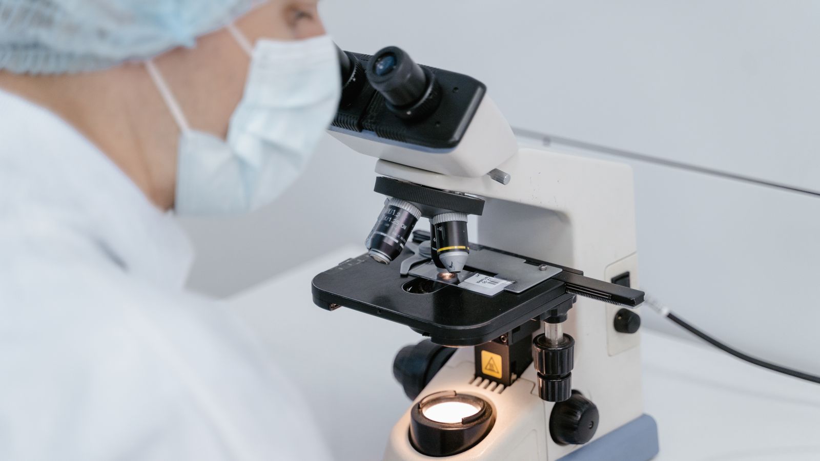 Scientist using a microscope in a laboratory setting, wearing protective gear.