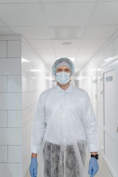 A healthcare worker in full protective gear stands in a sterile white hallway.