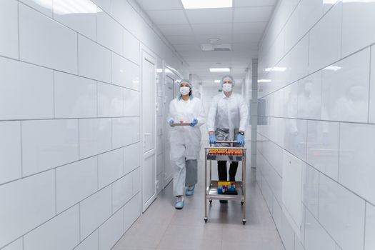 Two medical professionals with equipment in a sterile lab environment, ensuring safety and health protocols.
