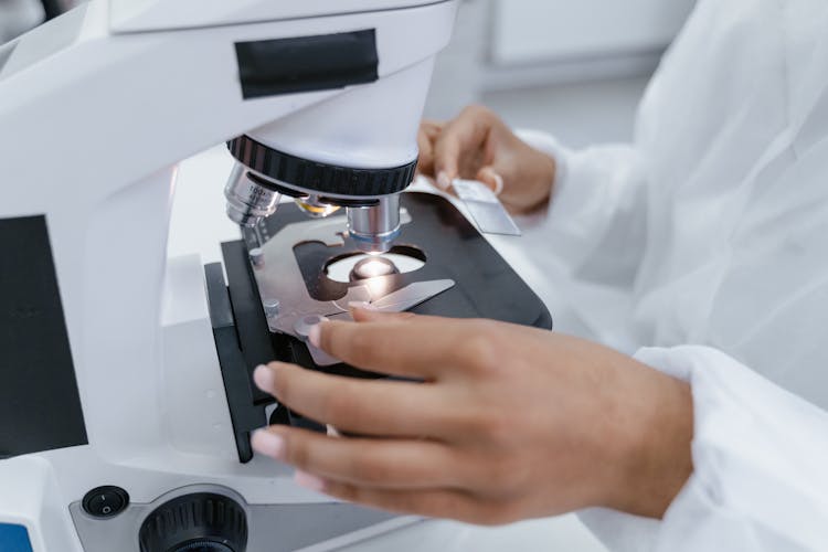 A Person In White Robe Using A Microscope