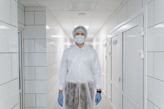 Healthcare worker in protective clothing standing in a sterile hospital corridor.