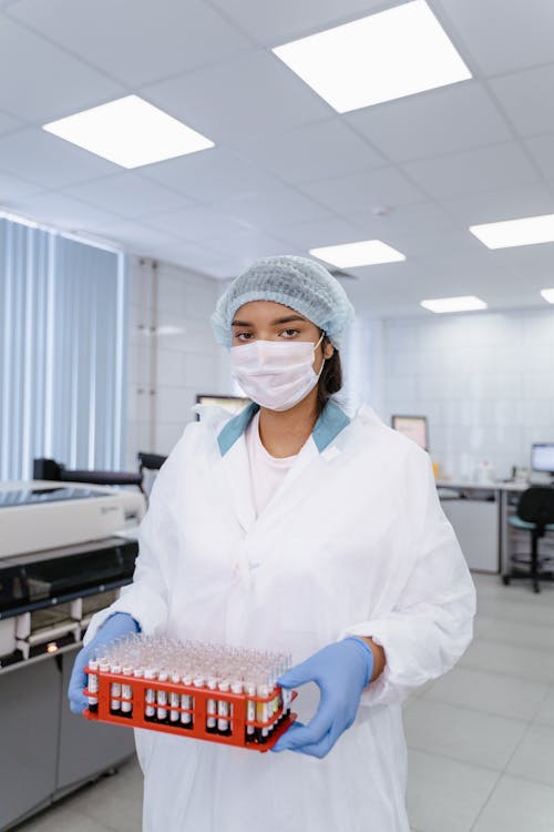 A Woman in White Lab Gown while Holding a Test Tube Rack