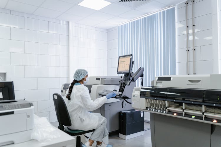 A Woman In White Lab Gown Sitting While Using The Computer