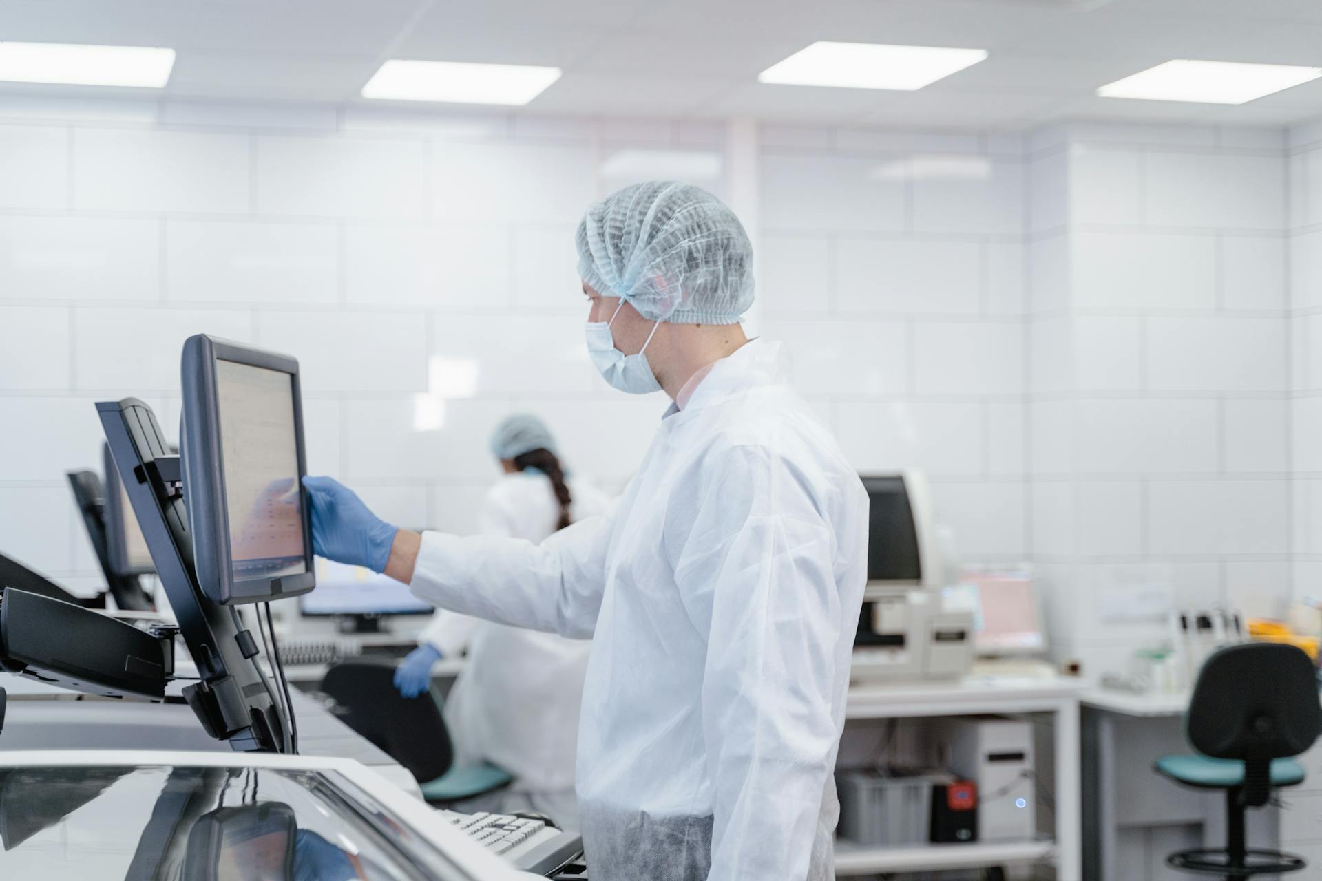 Scientist wearing protective gear while interacting with lab equipment and screen.