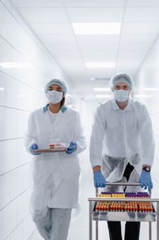 Medical staff in protective gear handling samples in a laboratory corridor.