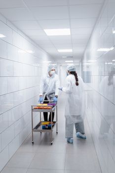Two scientists in protective clothing handling vials in a lab hallway.