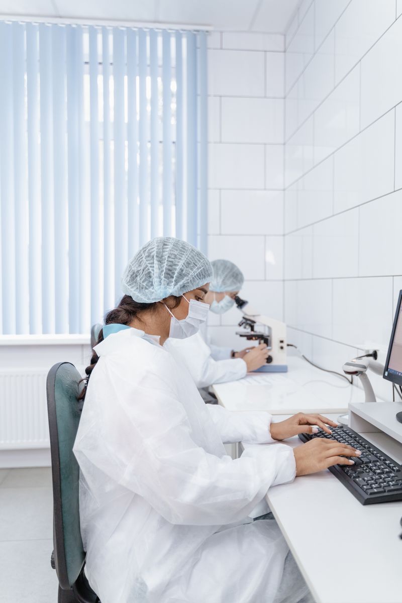 Two scientists in PPE typing on computers in a laboratory environment.