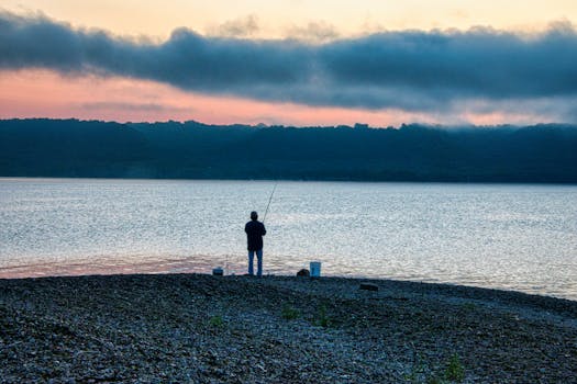 A lone fisherman at sunrise on the serene shores of Lake City, MN, casting a line into the tranquil waters.