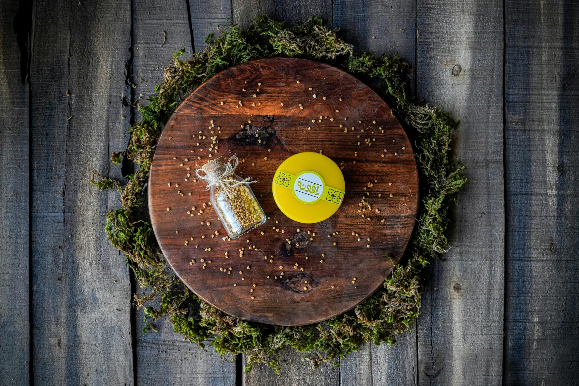 Aesthetic flat lay with a glass bottle of seeds on a wooden tray, surrounded by greenery.