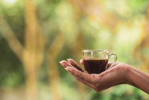 Close-up of a hand holding a glass cup of coffee with a blurred outdoor background.. close, hand, holding