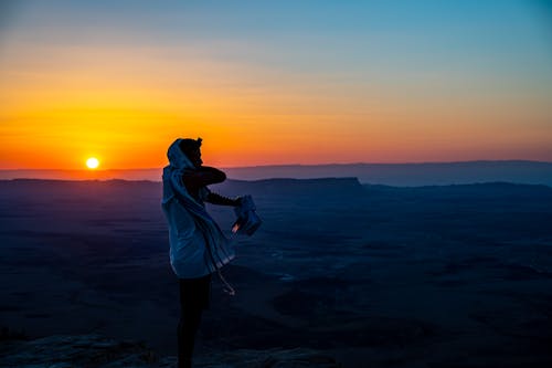 Woman in White Jacket Standing on Rock Formation during Sunset