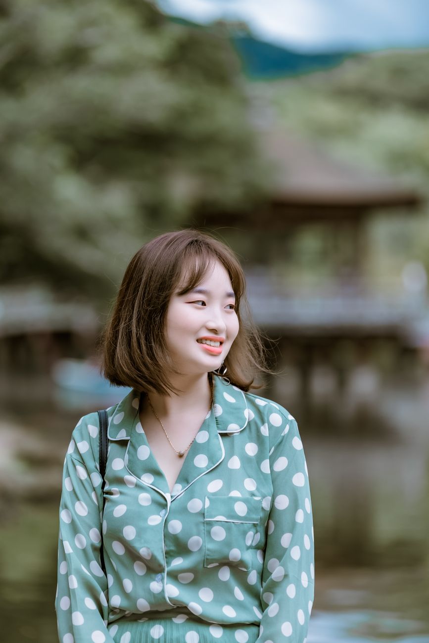 Young woman smiling outdoors in polka dot dress, enjoying a sunny day.