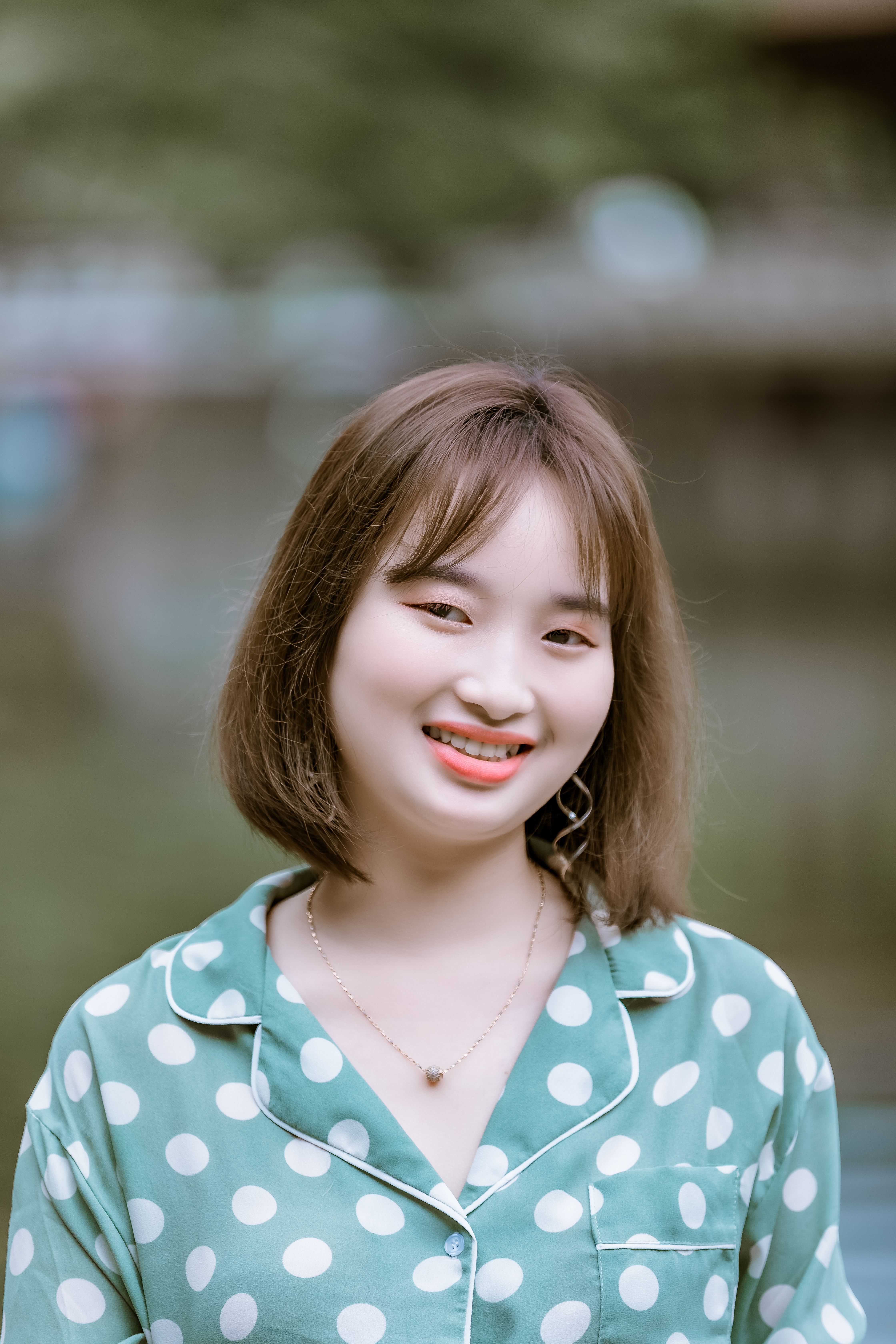 Young woman with a cheerful smile wearing a polka dot shirt outdoors.
