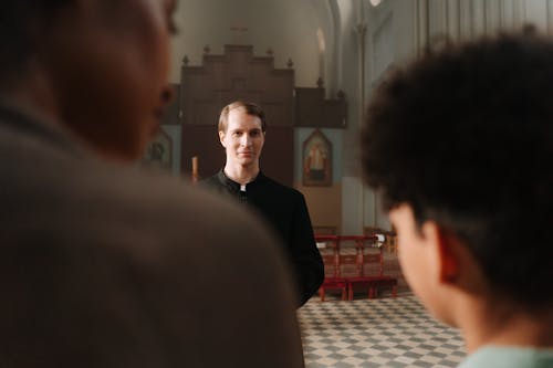 A Priest in Cassock Looking at the People inside a Church