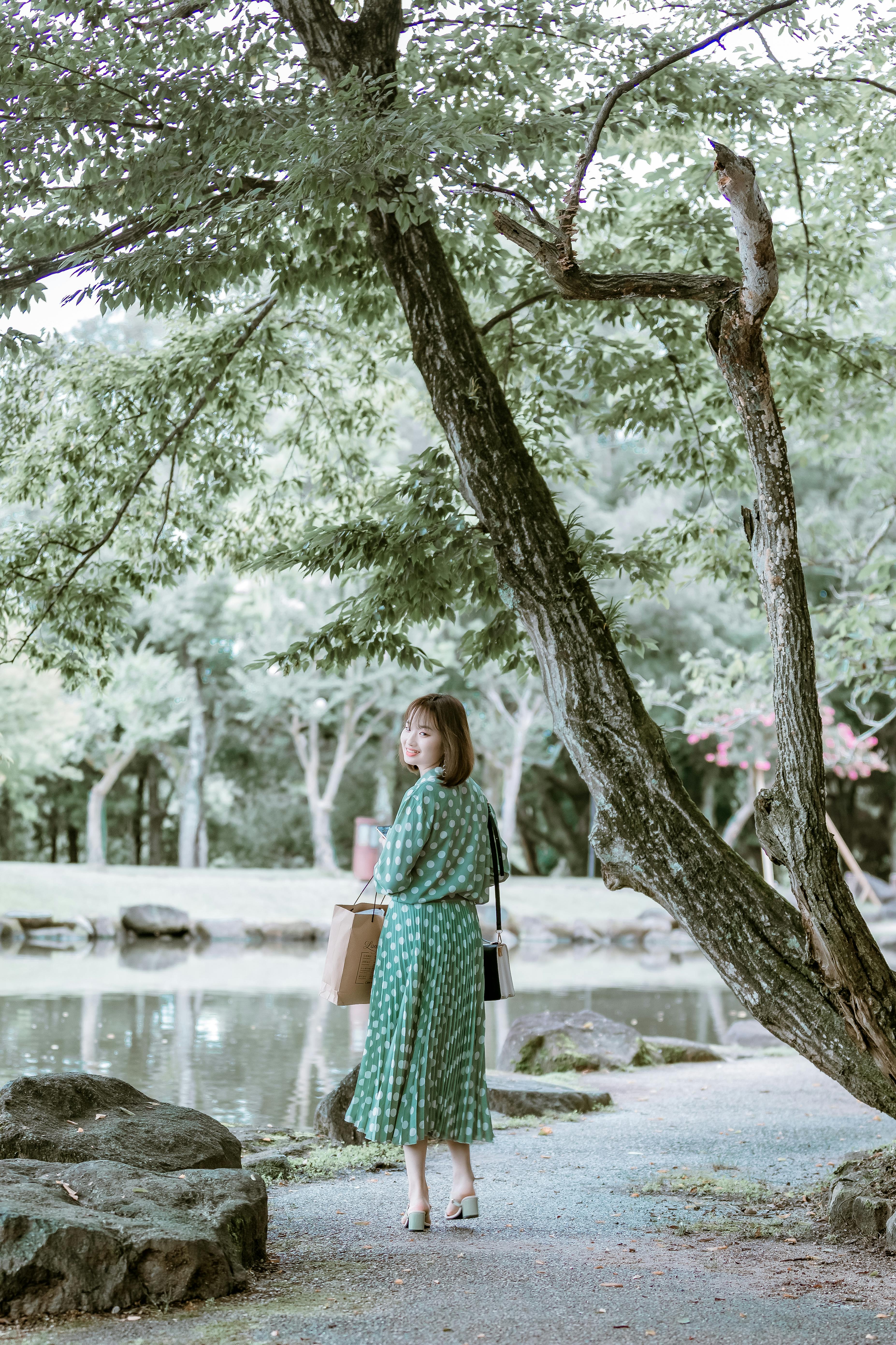 Free Stylish Asian woman enjoys a serene walk in a lush green park. Stock Photo