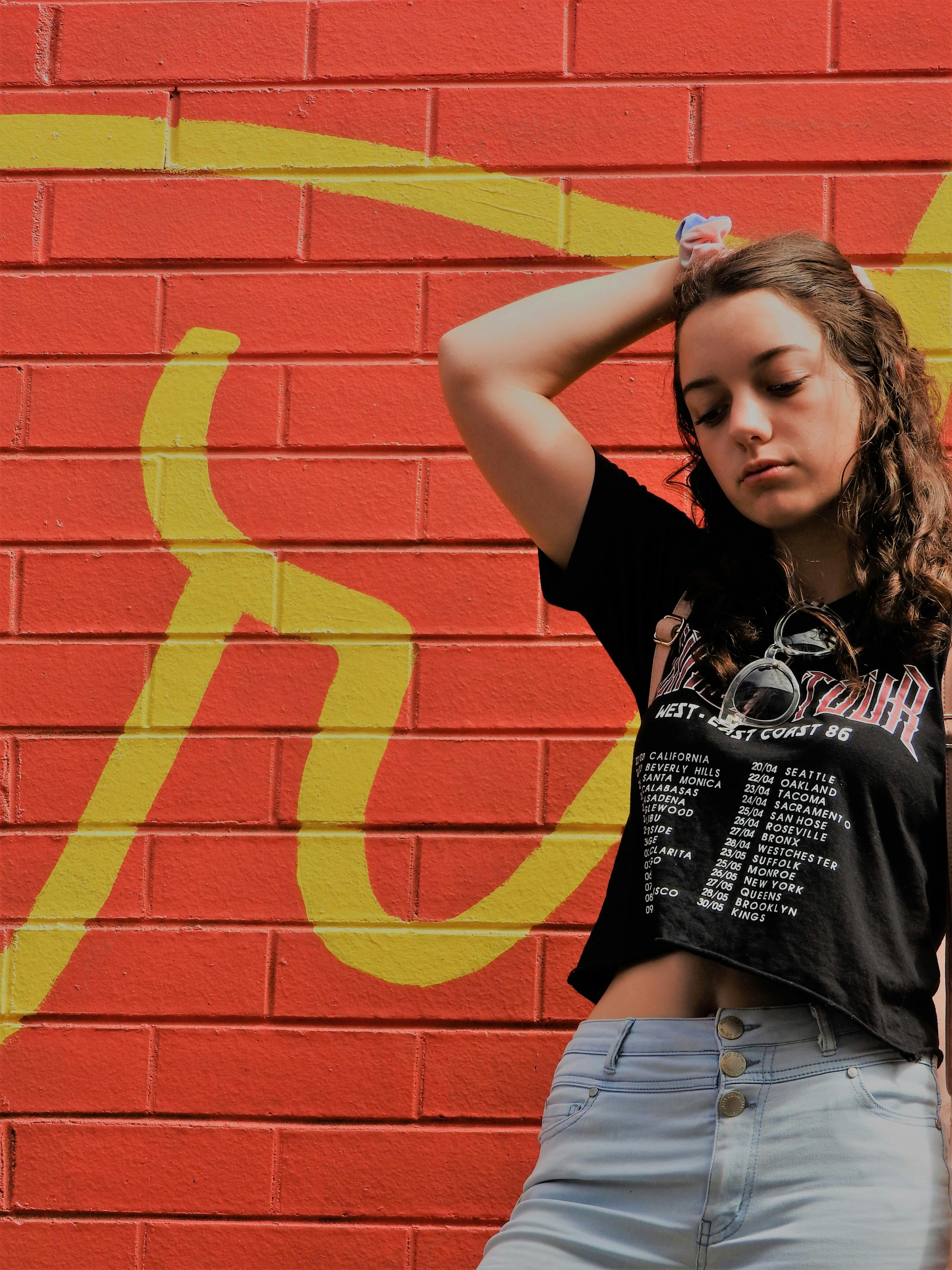 一位时尚的年轻女子在色彩缤纷的涂鸦砖墙前随意摆着姿势