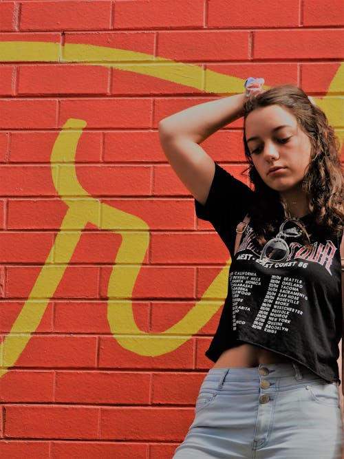 Vrouw In Zwart Shirt En Blauwe Bodems Die Zich Dichtbij Rode Muur Bevinden