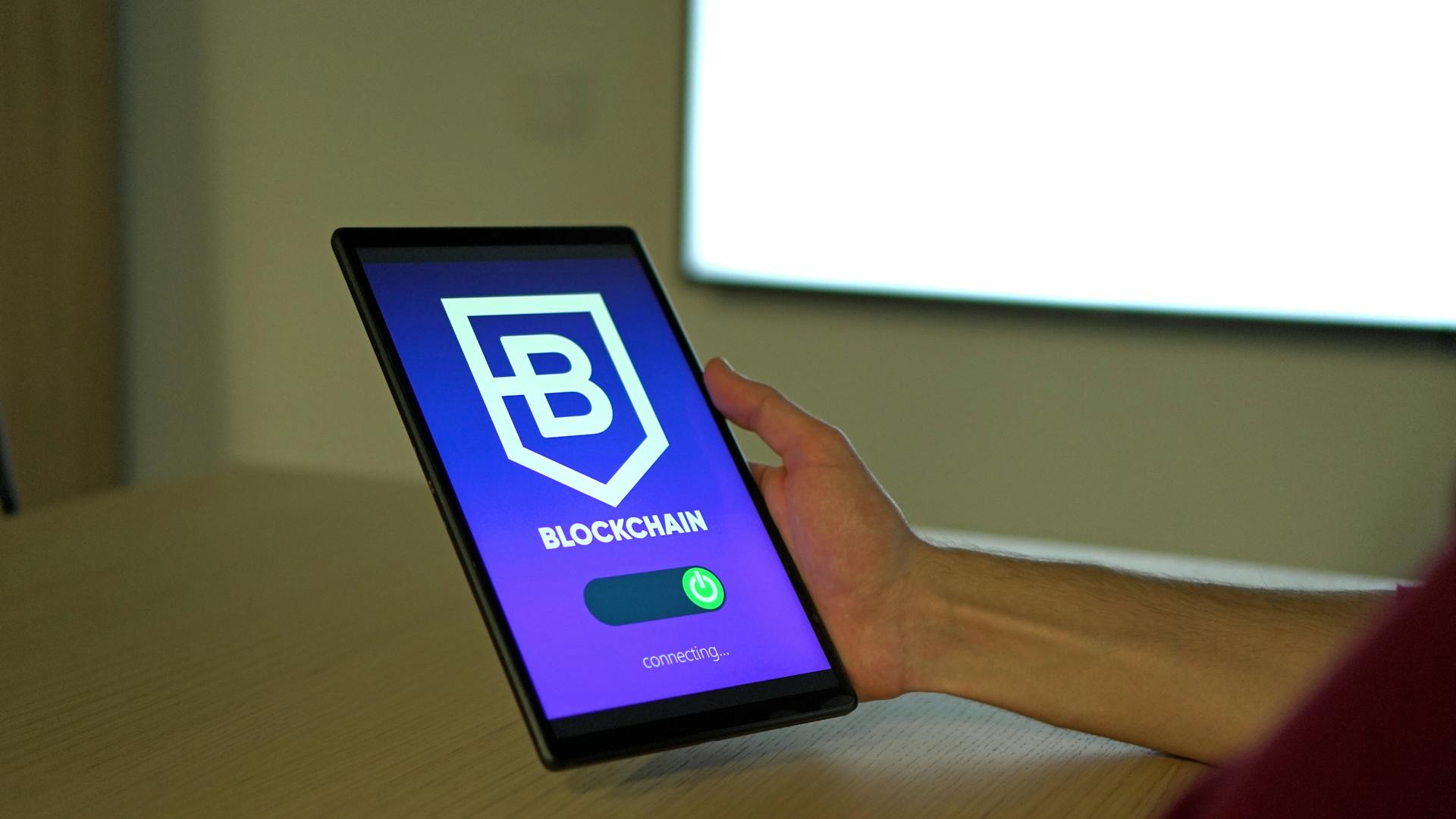 A hand holding a tablet with blockchain logo on screen, showcasing digital technology.