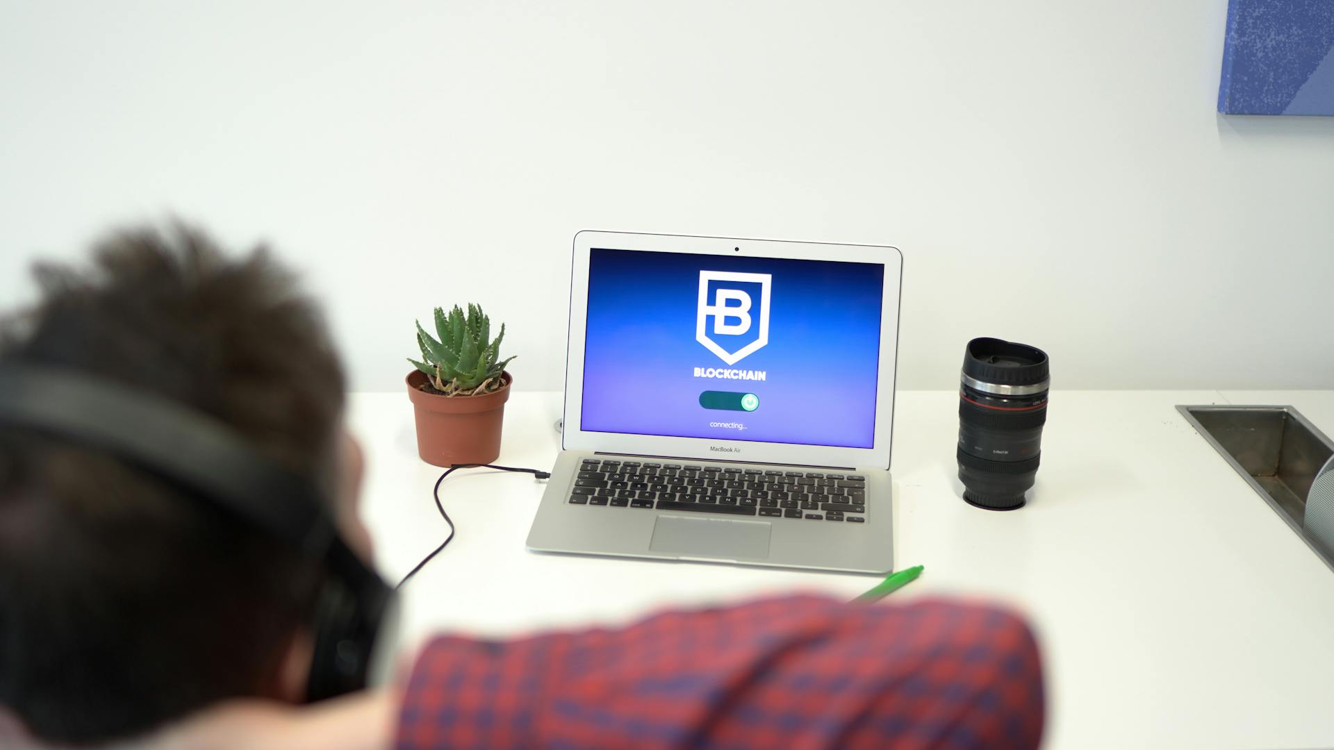 A person wearing headphones viewing a blockchain screen on a laptop, indoor setting.