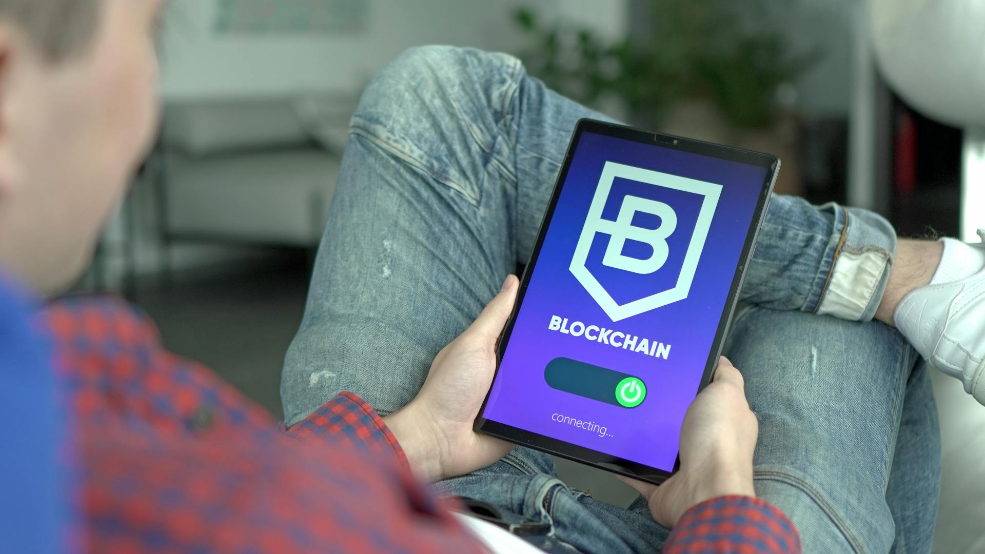 Adult holding a digital tablet displaying a blockchain application interface.