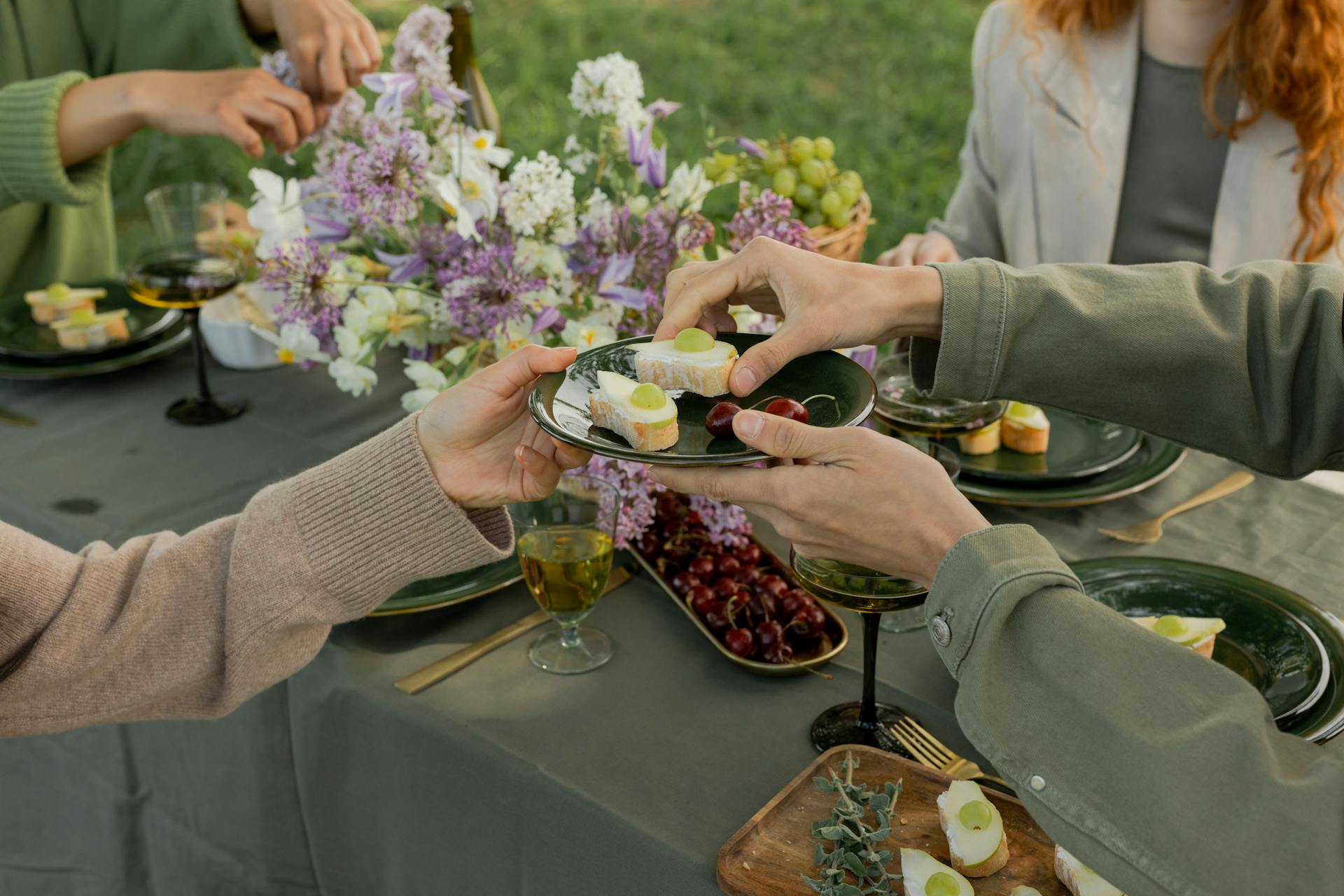 A group of friends enjoying a picnic with cheese and wine in a lush outdoor setting.