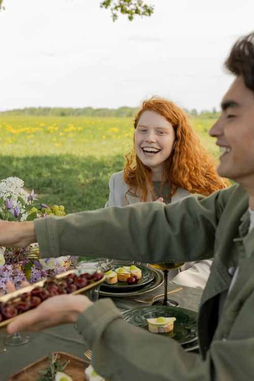 Free Friends enjoying a joyful picnic in a sunny field, sharing food and laughter. Stock Photo