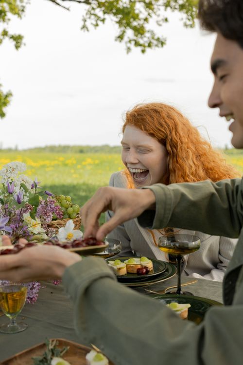 Free Happy friends sharing laughter and food during a scenic outdoor picnic. Stock Photo