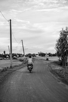 A lone motorcyclist rides down a rural dirt road, showcasing the serenity of the countryside.