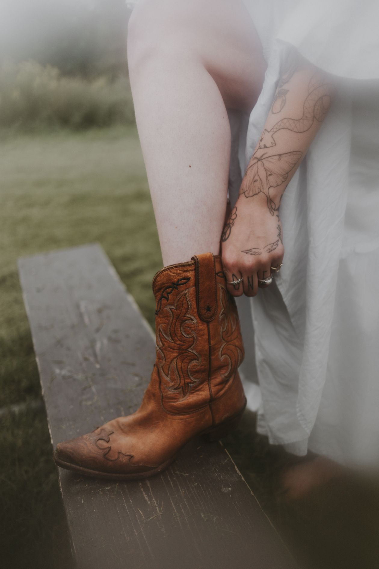 Person adjusting a tooled brown leather cowboy boot while seated outdoors