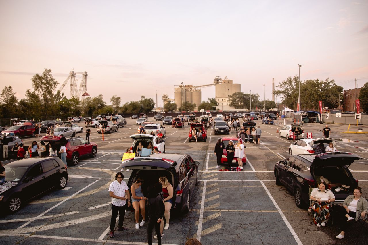 People gathering around cars in an open lot under a wide sky — photo by Wendy Wei on Pexels